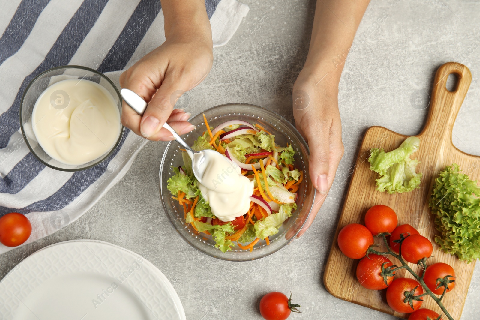 Photo of Woman adding mayonnaise to delicious salad at grey table, top view