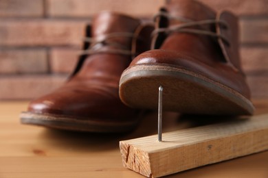 Photo of Metal nail in wooden plank and shoes on table, closeup