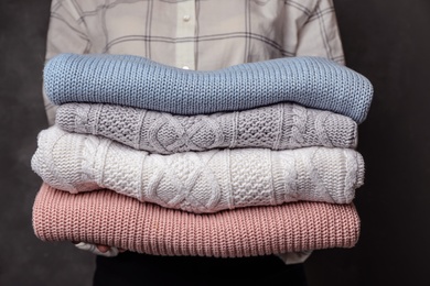 Photo of Woman holding stack of folded warm knitted sweaters, closeup