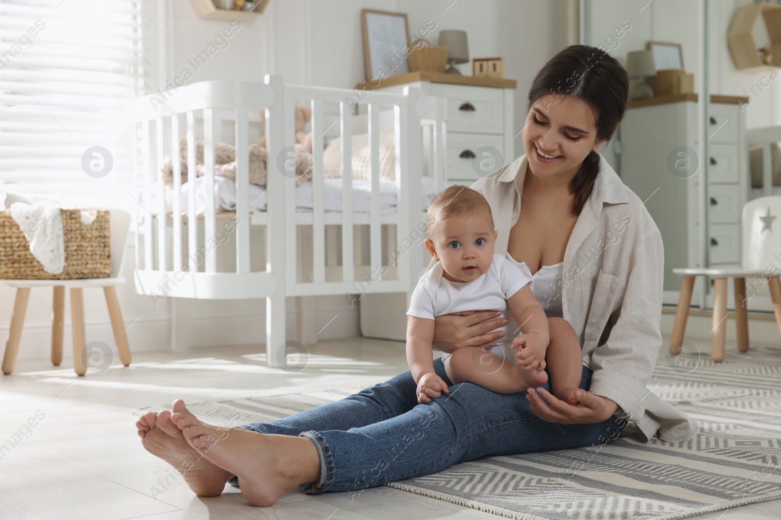 Photo of Happy young mother with her baby in nursery. Space for text