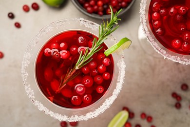 Photo of Tasty cranberry cocktail with rosemary and lime in glasses on grey table, flat lay