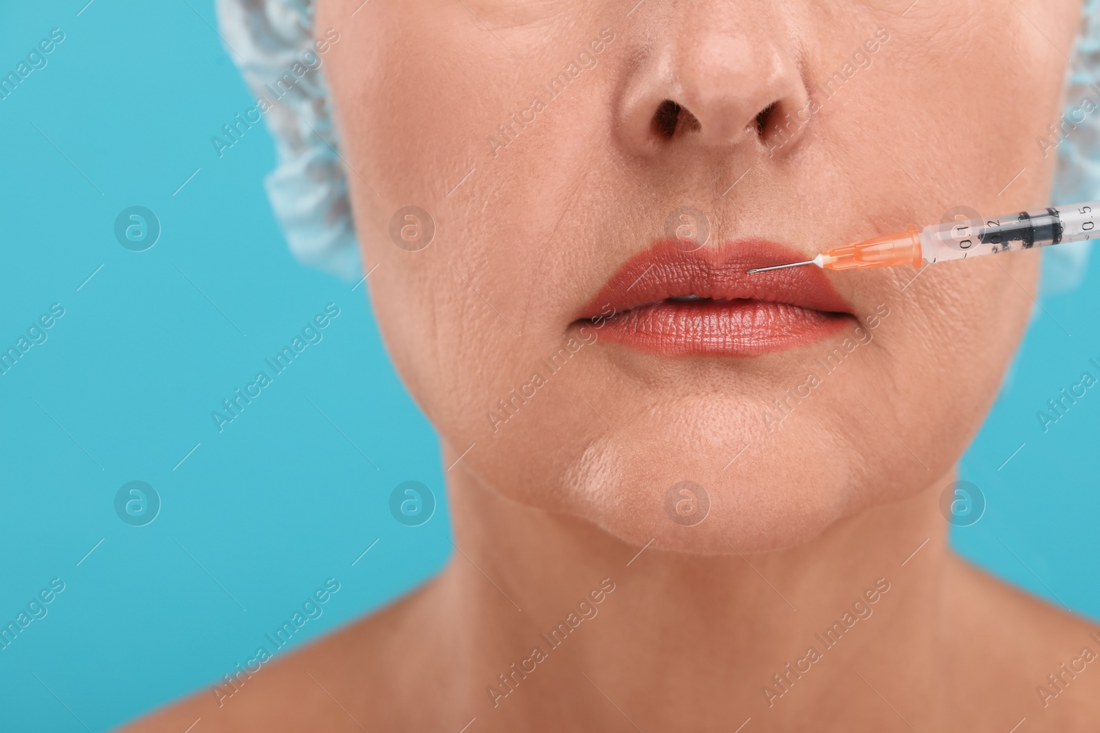 Photo of Senior woman getting lips injection on light blue background, closeup. Cosmetic surgery