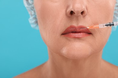 Senior woman getting lips injection on light blue background, closeup. Cosmetic surgery