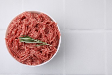 Fresh raw ground meat and rosemary in bowl on white tiled table, top view. Space for text