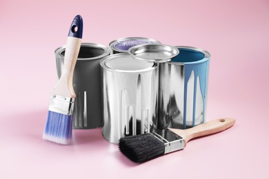 Photo of Cans of paints and brushes on pink background