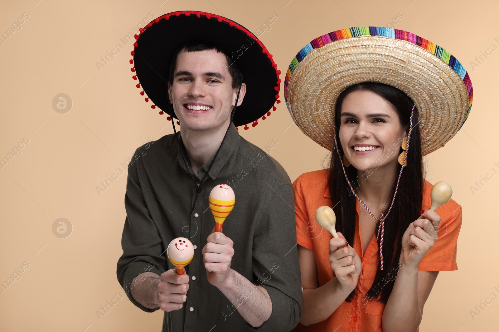 Photo of Lovely couple woman in Mexican sombrero hats with maracas on beige background