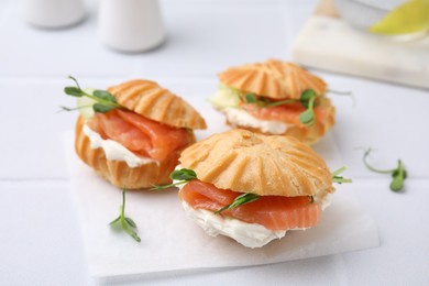 Delicious profiteroles with cream cheese and salmon on white table, closeup