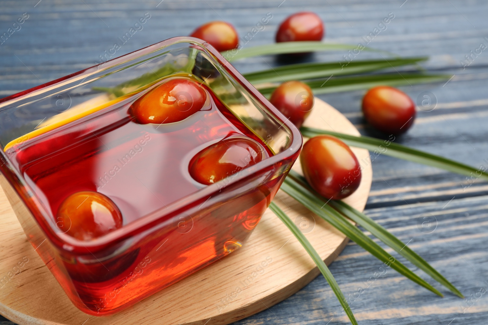 Photo of Palm oil in glass bowl with fruits and tropical leaf on blue wooden table, closeup