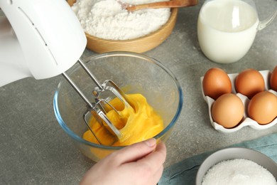 Photo of Woman beating eggs with mixer at light grey table, closeup