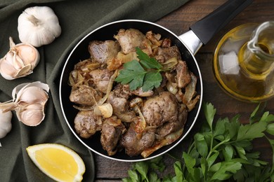 Photo of Tasty fried chicken liver with onion and parsley served on wooden table, flat lay