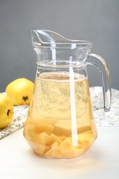 Photo of Delicious quince drink in glass jug and fresh fruits on white wooden table