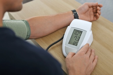 Photo of Man checking blood pressure with sphygmomanometer at table indoors, closeup. Cardiology concept