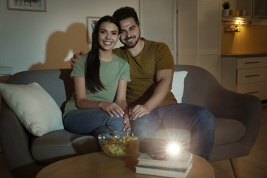 Photo of Young couple watching movie using video projector at home
