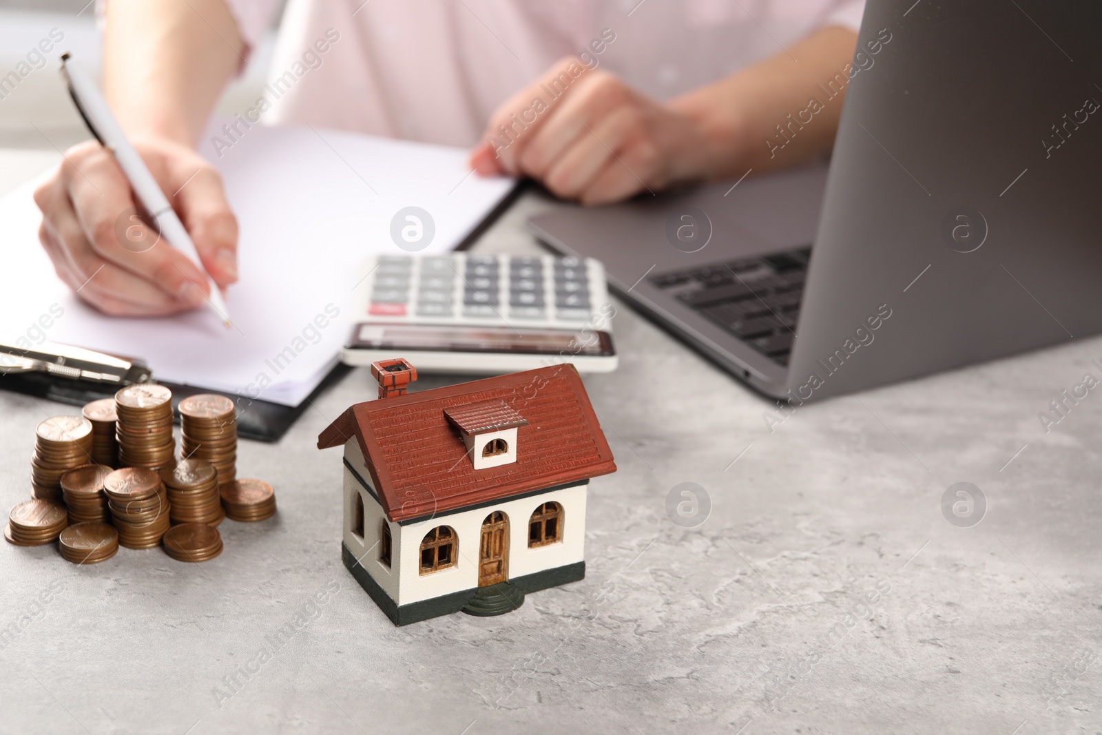 Photo of Woman planning budget at grey table, focus on house model and coins