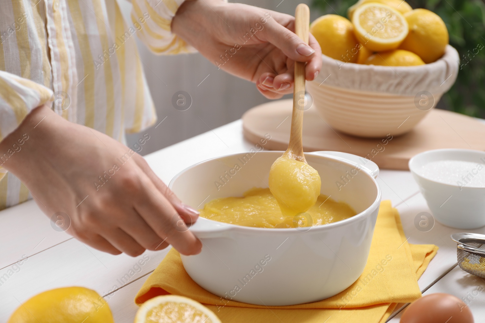 Photo of Woman cooking lemon curd at white wooden table, closeup