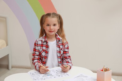Little girl coloring antistress page at table indoors