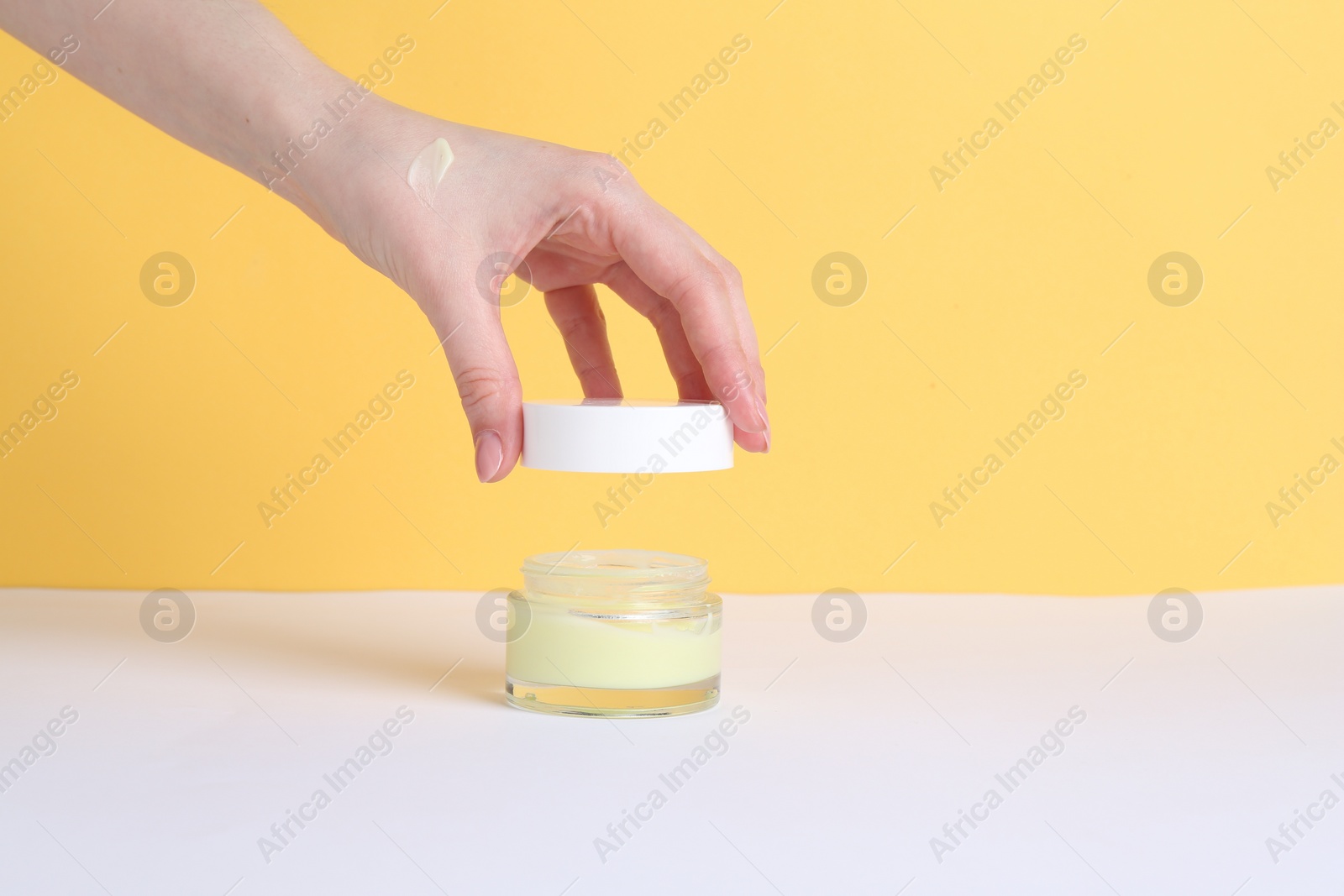 Photo of Woman with jar of cream on yellow background, closeup