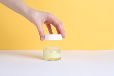 Woman with jar of cream on yellow background, closeup