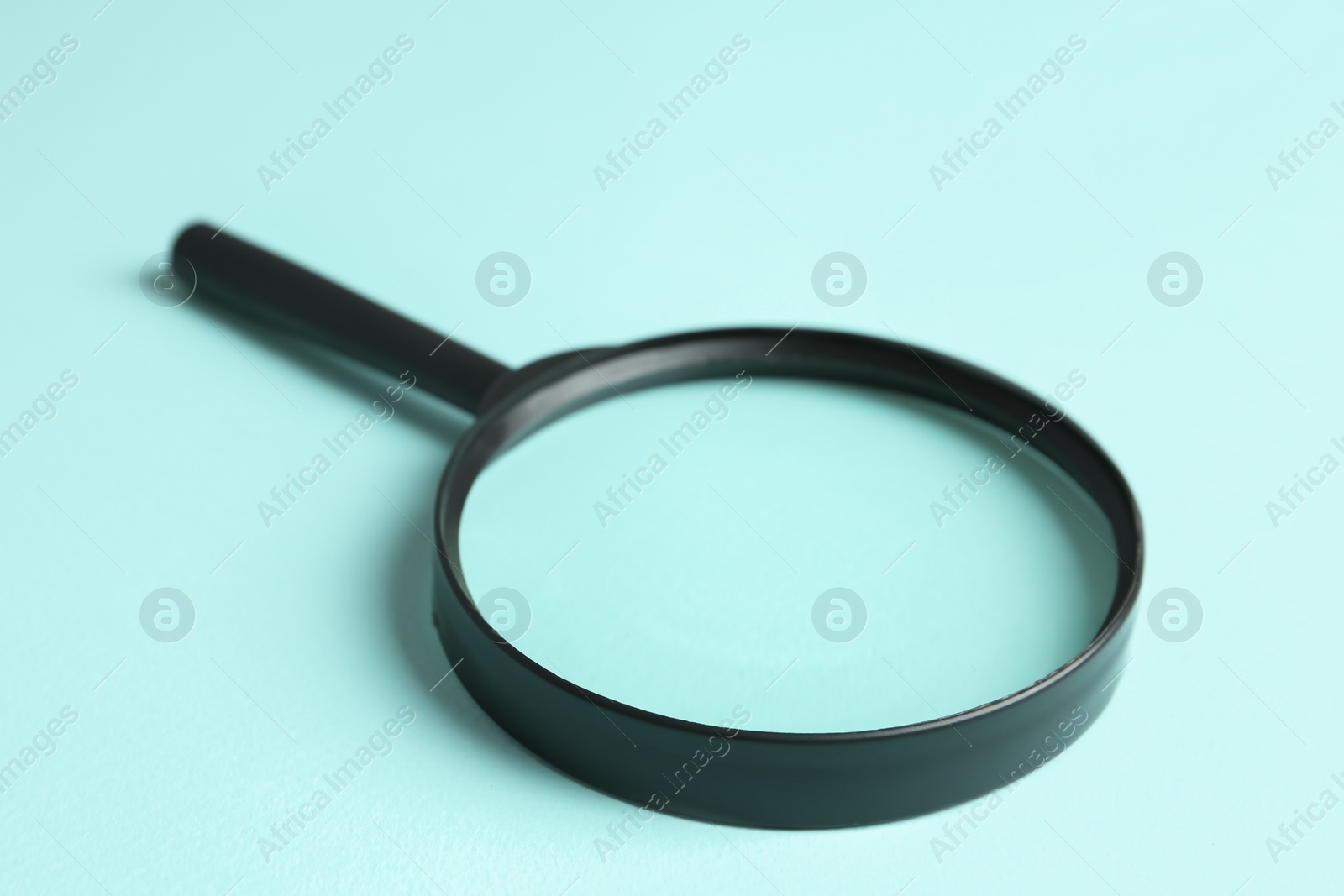 Photo of Magnifying glass on light blue background, closeup. Search concept