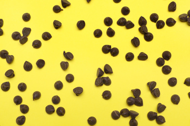 Delicious chocolate chips on yellow background, top view