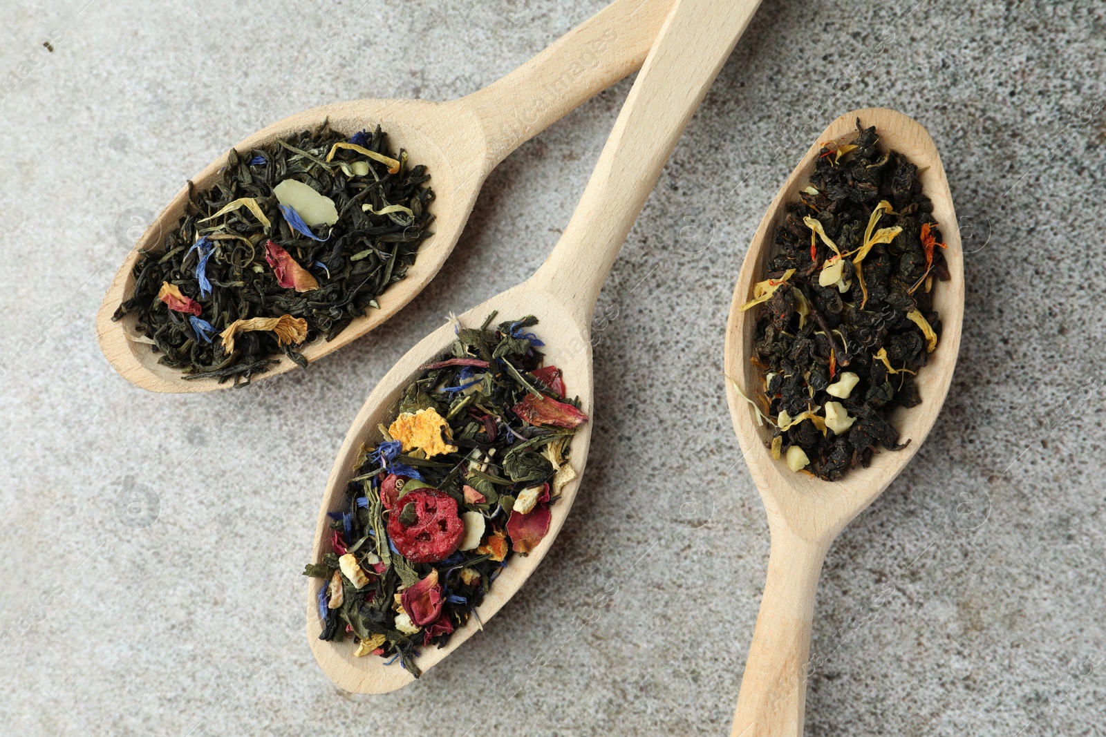 Photo of Different kinds of dry herbal tea in wooden spoons on light grey table, flat lay