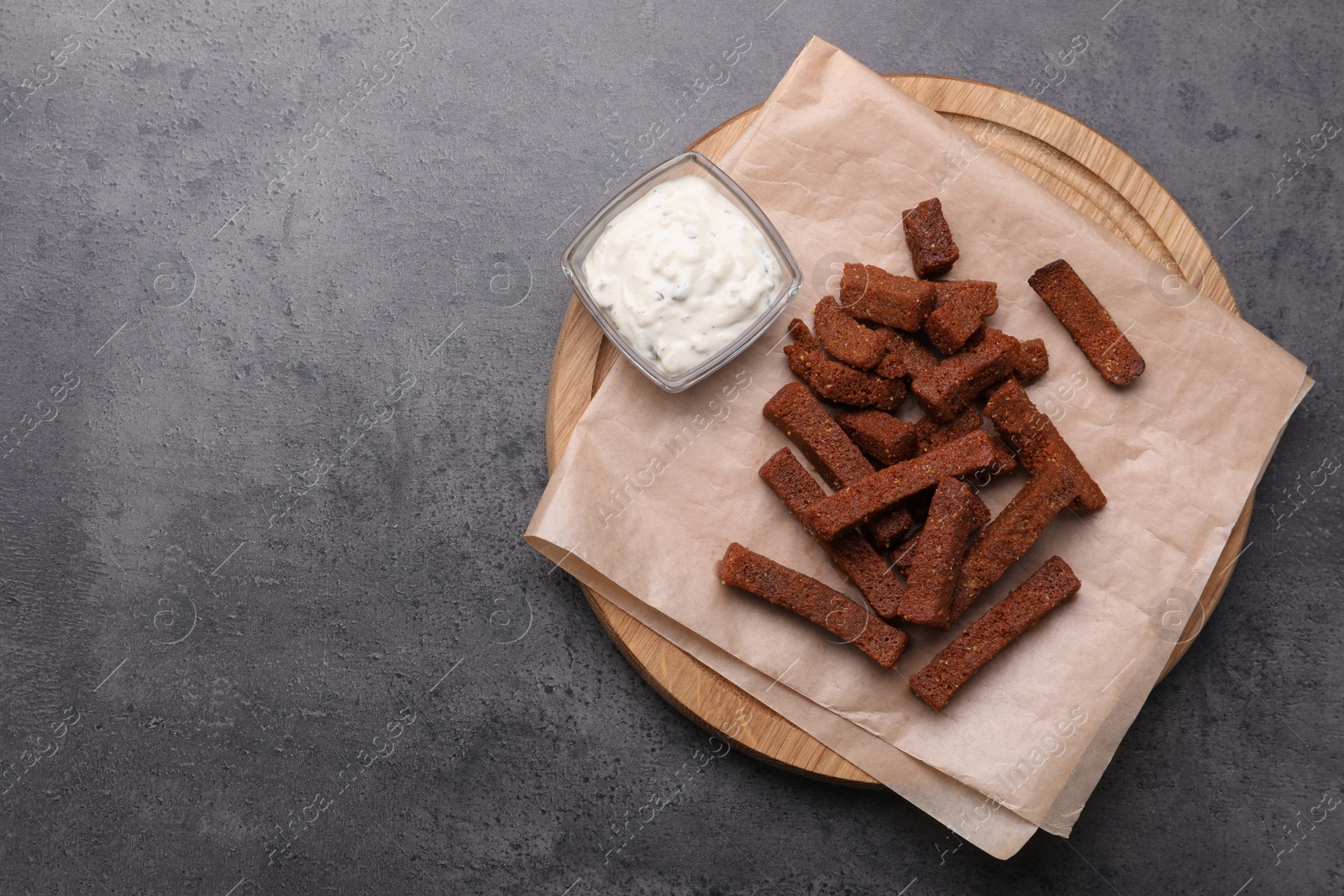 Photo of Wooden board with crispy rusks and dip sauce on grey table, top view. Space for text