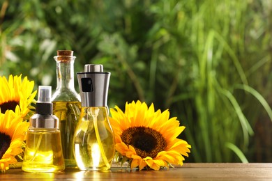 Sunflowers and many different bottles with cooking oil on wooden table against blurred green background. Space for text