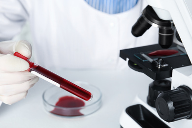 Photo of Scientist holding test tube with blood sample at table, closeup. Virus research