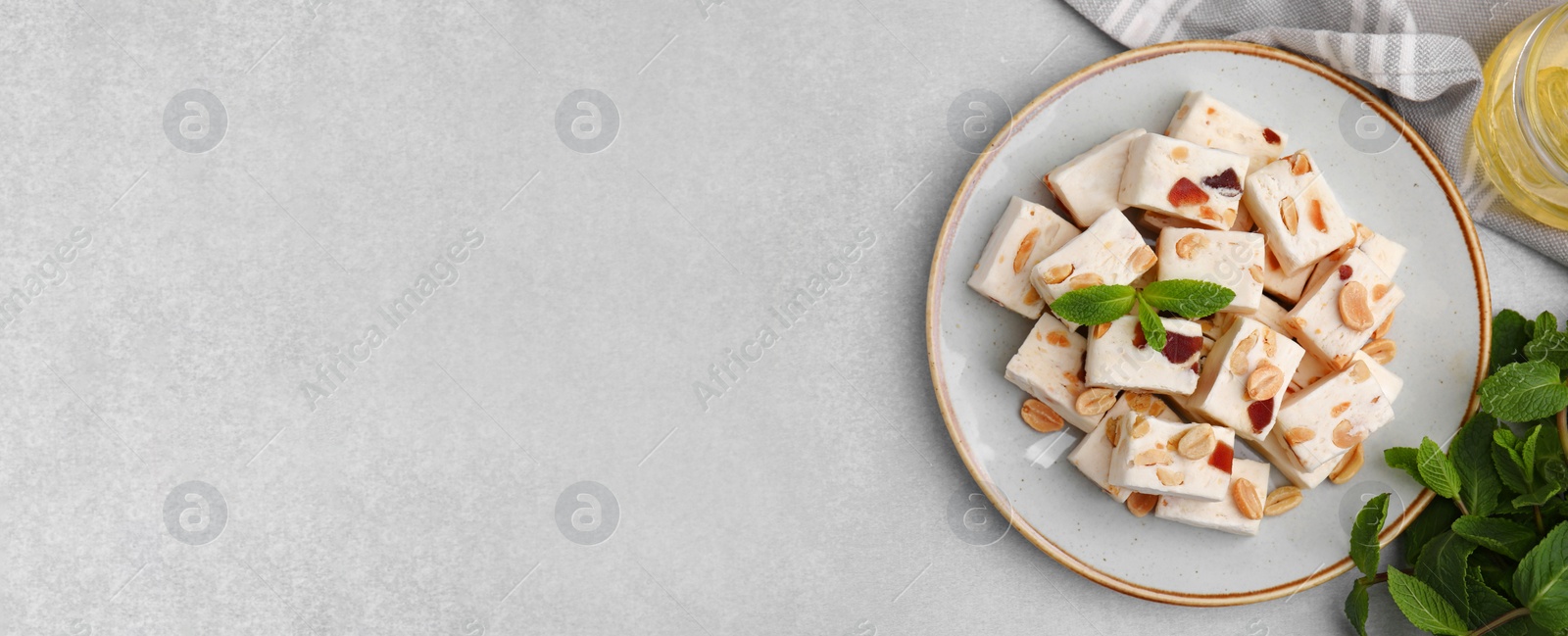 Image of Pieces of delicious nutty nougat and ingredients on light gray table, flat lay. Banner design with space for text