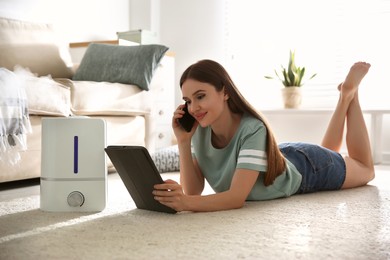 Photo of Woman using gadgets in room with modern air humidifier