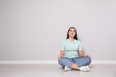 Photo of Young woman sitting on floor near light grey wall indoors. Space for text