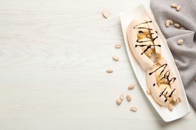 Photo of Delicious banana split ice cream portions with chocolate topping and peanuts on white wooden table, flat lay. Space for text