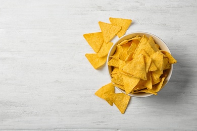 Photo of Tasty mexican nachos chips in bowl on white wooden table, flat lay. Space for text