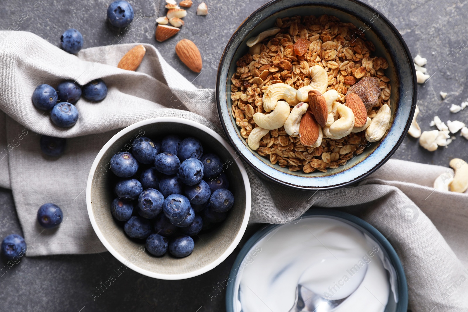 Photo of Tasty granola in bowl, blueberries, yogurt and spoon on gray textured table, flat lay