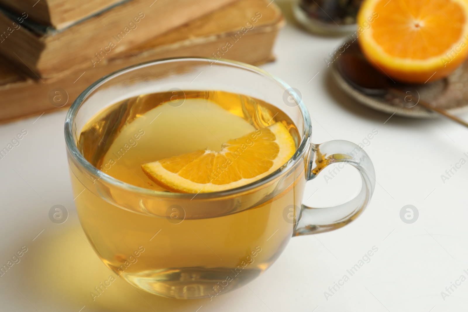 Photo of Glass cup of freshly brewed tea with orange on light table, closeup