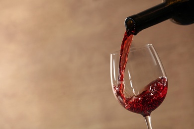 Photo of Pouring red wine into glass from bottle against blurred beige background, closeup. Space for text