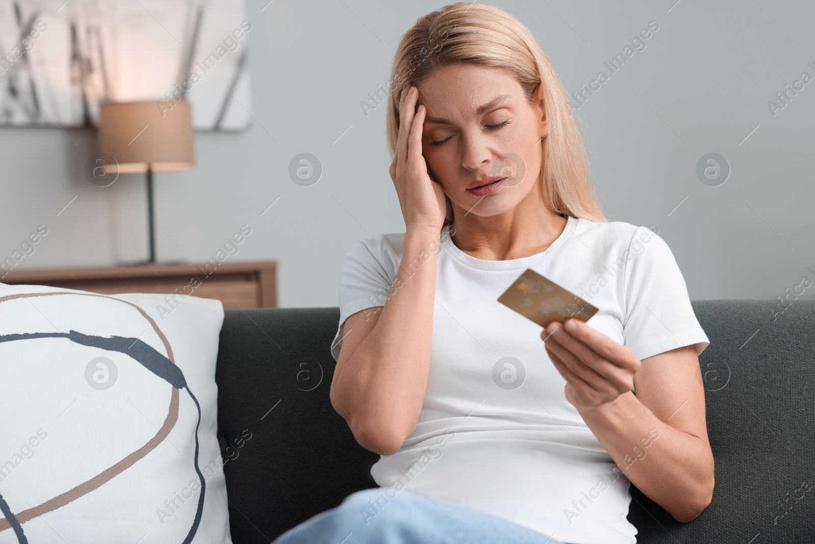 Photo of Stressed woman with credit card on sofa at home. Be careful - fraud