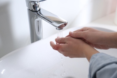 Photo of Woman putting burned hand under running cold water indoors, closeup