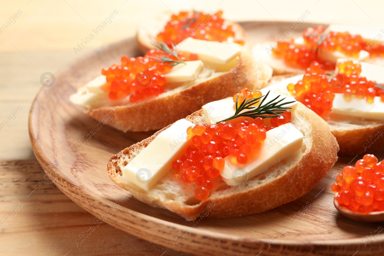 Photo of Delicious sandwiches with red caviar on wooden plate, closeup