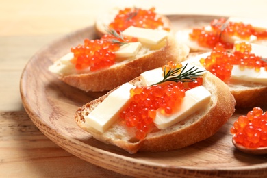 Photo of Delicious sandwiches with red caviar on wooden plate, closeup