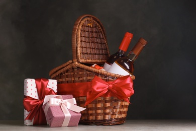 Photo of Festive basket with bottles of wine and gifts on table against dark background