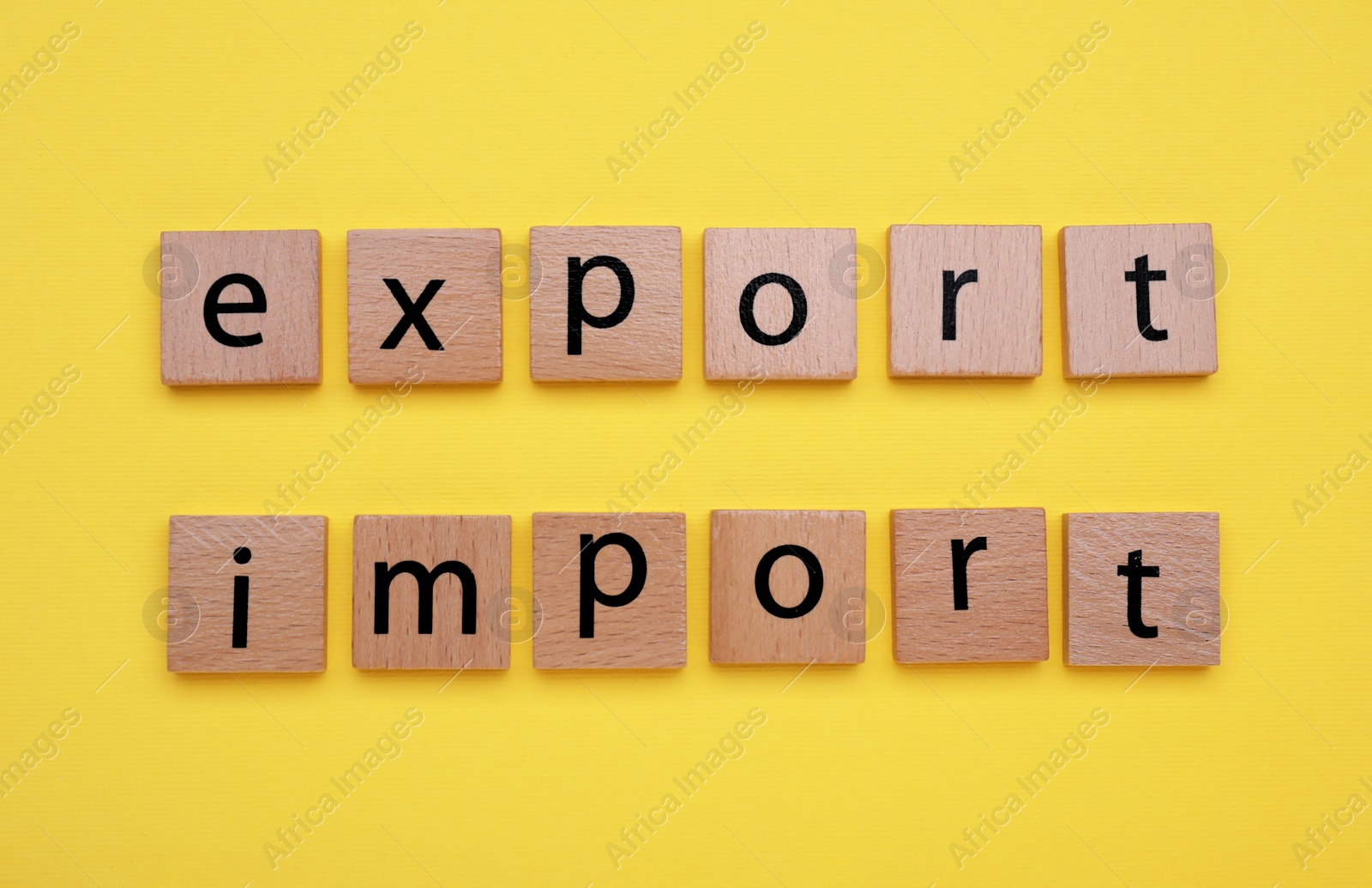 Photo of Words Import and Export made of wooden squares with letters on yellow background, top view