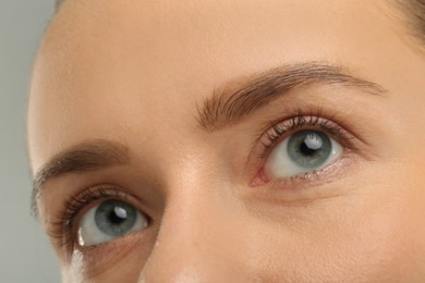 Woman with beautiful natural eyelashes on grey background, closeup