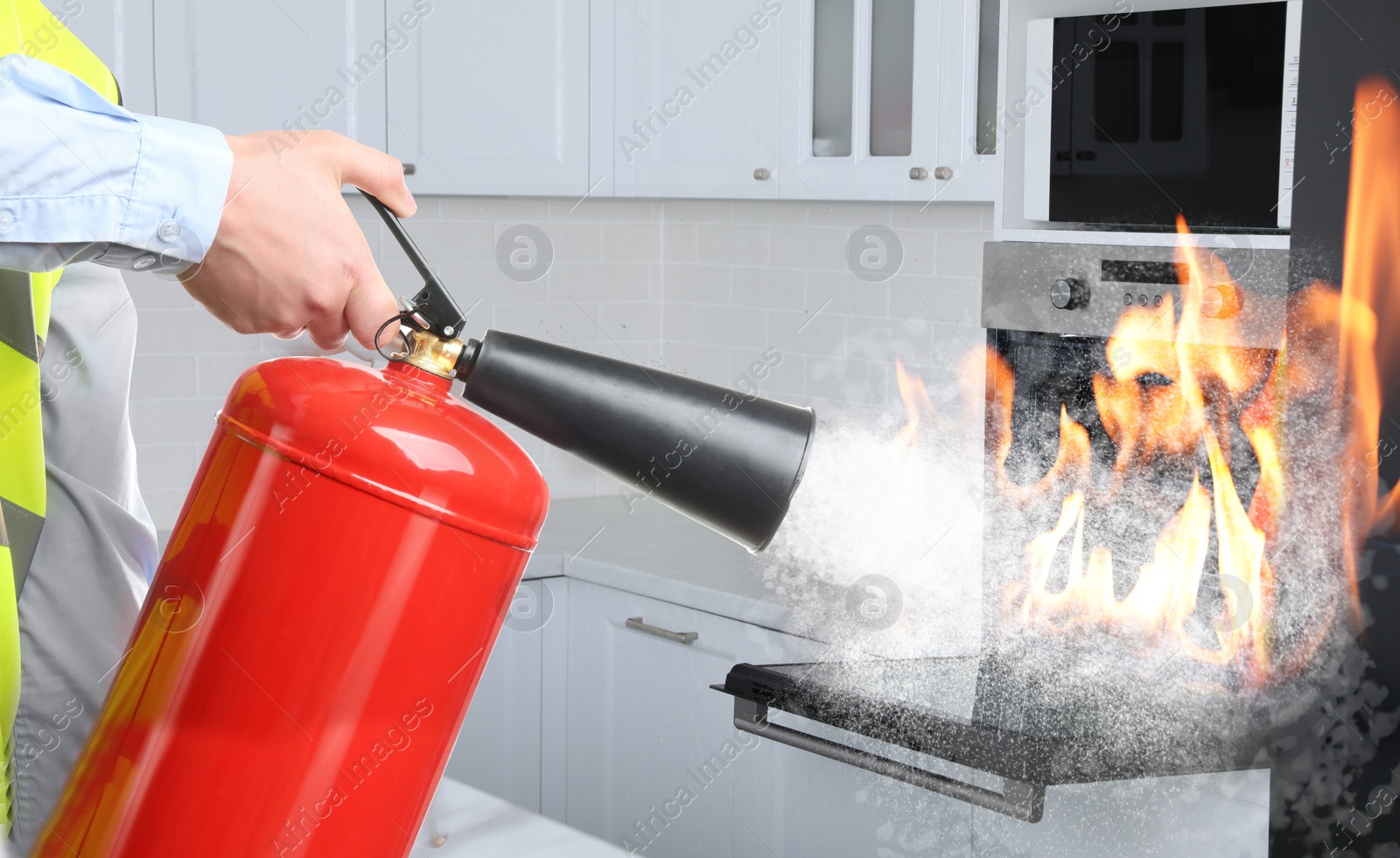 Image of Man putting out burning oven with fire extinguisher in kitchen, closeup