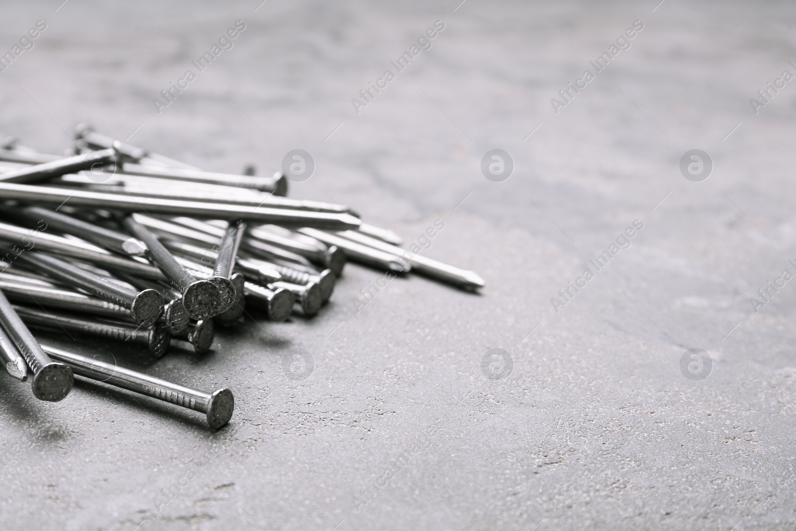 Photo of Pile of metal nails on grey stone background, closeup. Space for text