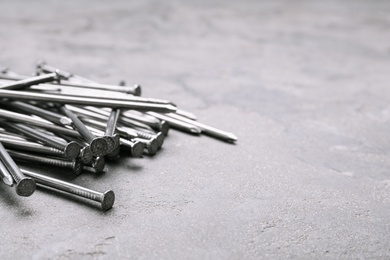 Photo of Pile of metal nails on grey stone background, closeup. Space for text