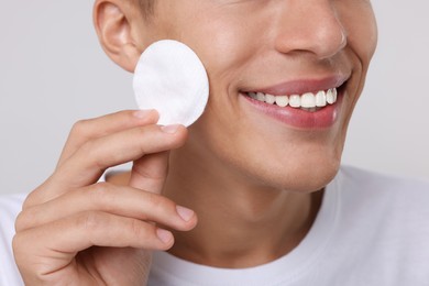 Photo of Man cleaning face with cotton pad on light background, closeup