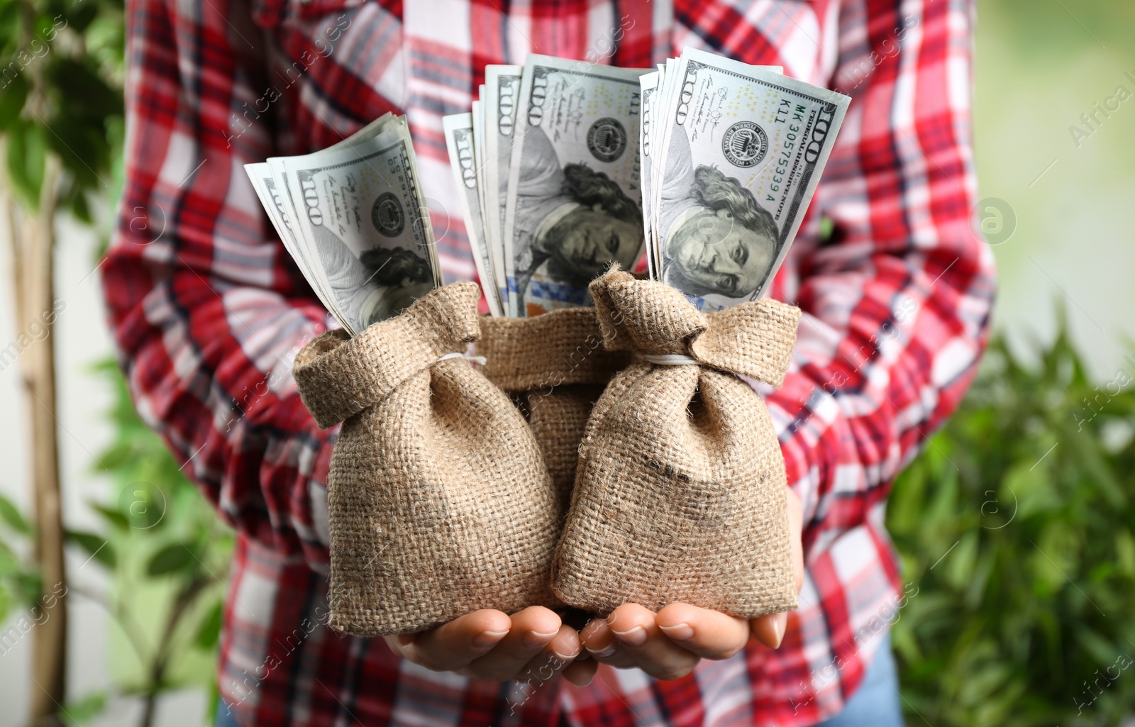 Photo of Woman holding sacks with dollars on blurred background, closeup. Money savings