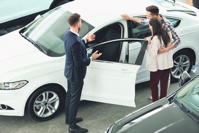 Photo of Young couple buying new car in salon