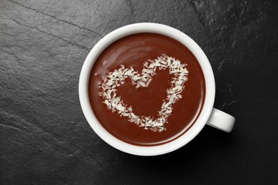 Cup of hot chocolate with heart shaped decoration on black table, top view